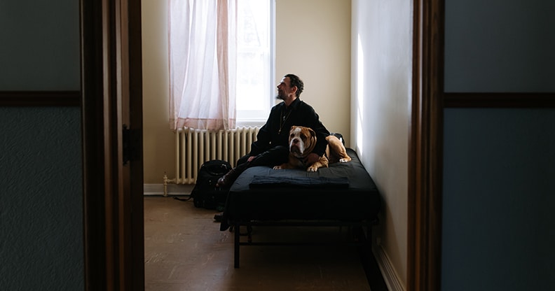 Un homme et son chien assis sur un lit dans une chambre sombre